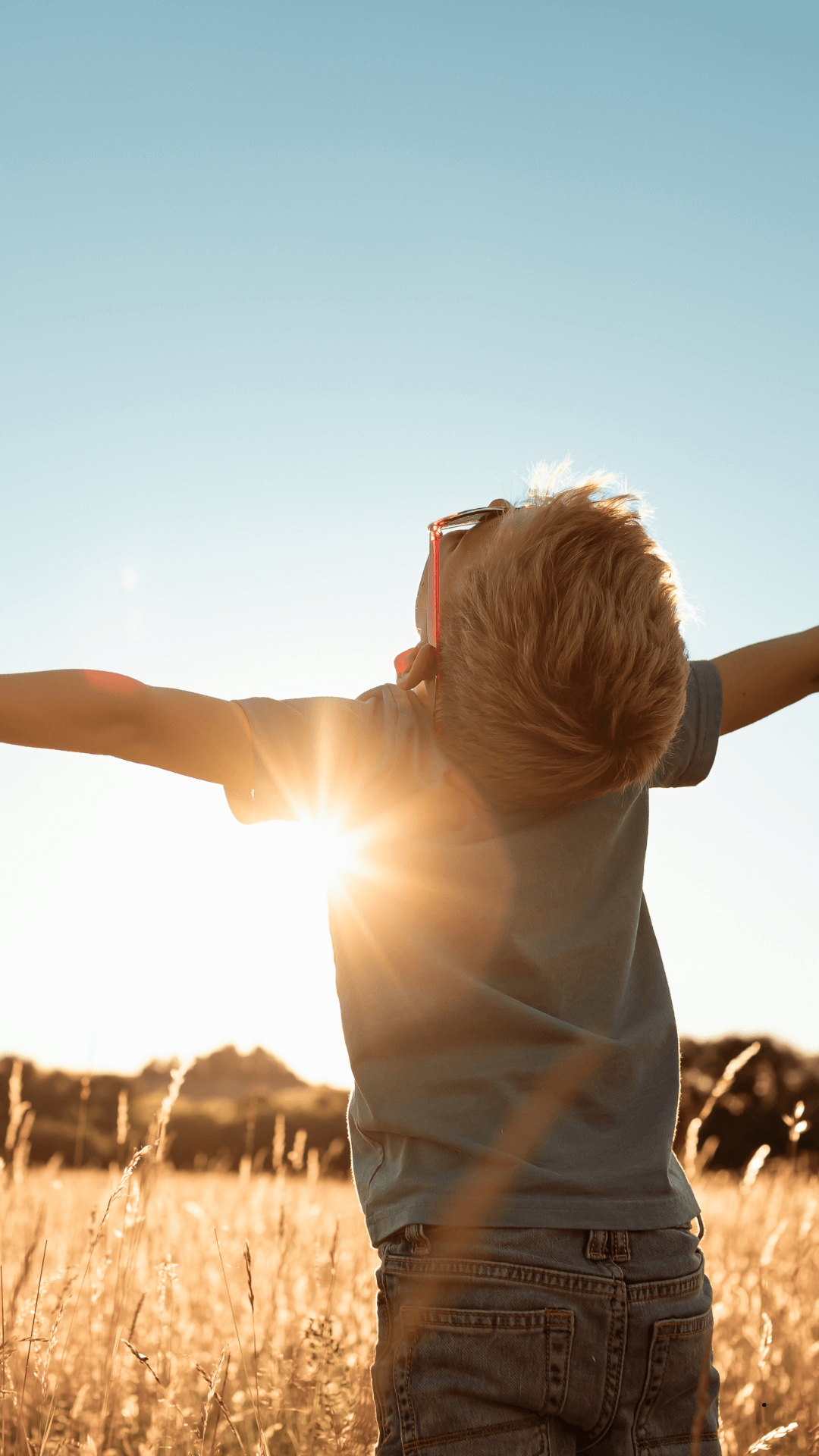 Freiheit und Lebensfreude – innere Stärke und positive Entwicklung Kind steht mit ausgebreiteten Armen in einer sonnigen Wiese und genießt Freiheit, Leichtigkeit und Natur